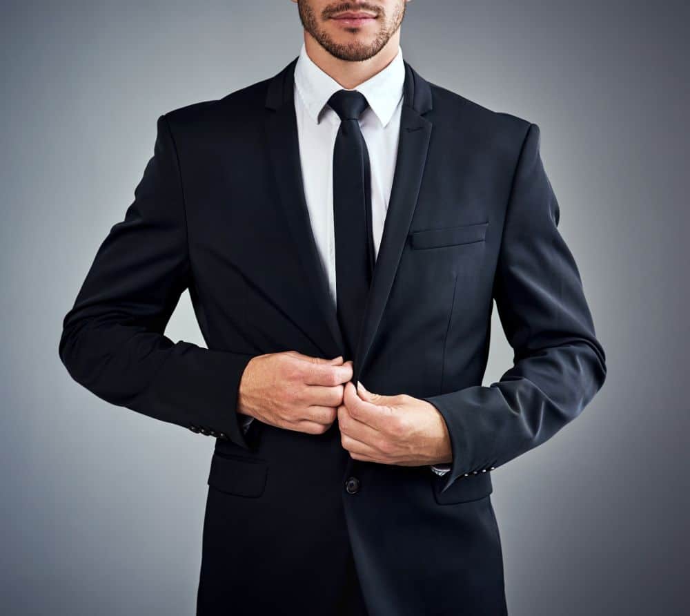 A man in a tailored black suit and tie adjusts his jacket