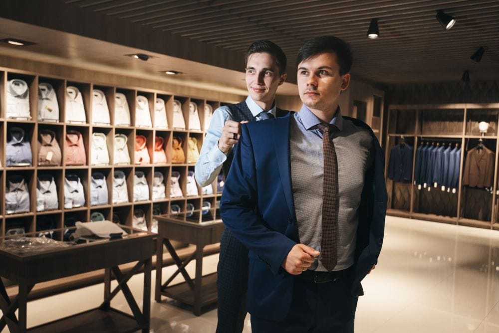 Tailor helps a patron try on their newly-finished suit
