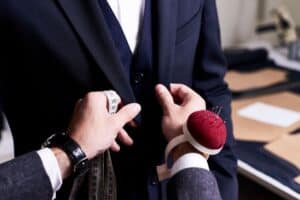 tailor holding measuring tape and pins while making adjustments on a suit