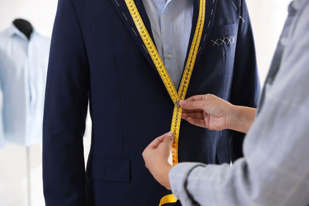 man gets fitted for a suit by a tailor using yellow tailors’ tape