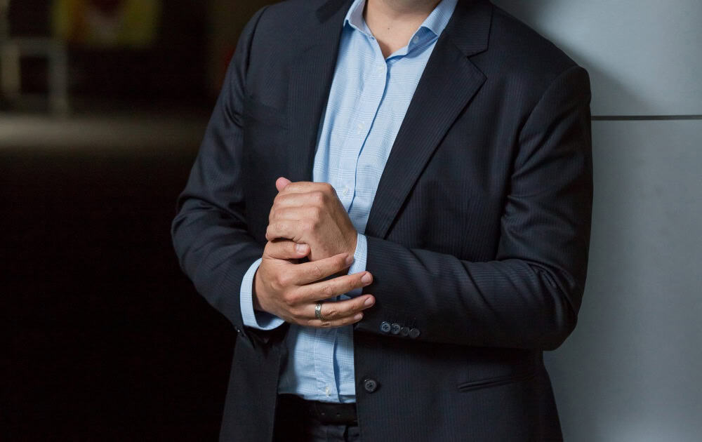 A man in a dark suit adjusting his cuff with his shirt tucked in neatly