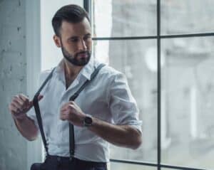 dapper man tugs at his suspenders while looking away