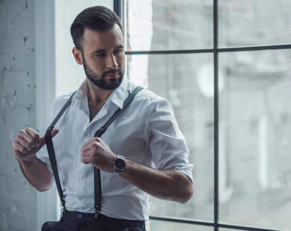 dapper man tugs at his suspenders while looking away