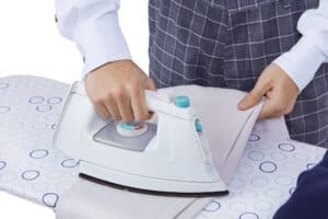 man uses an iron to get the wrinkles out of his linen suit pants