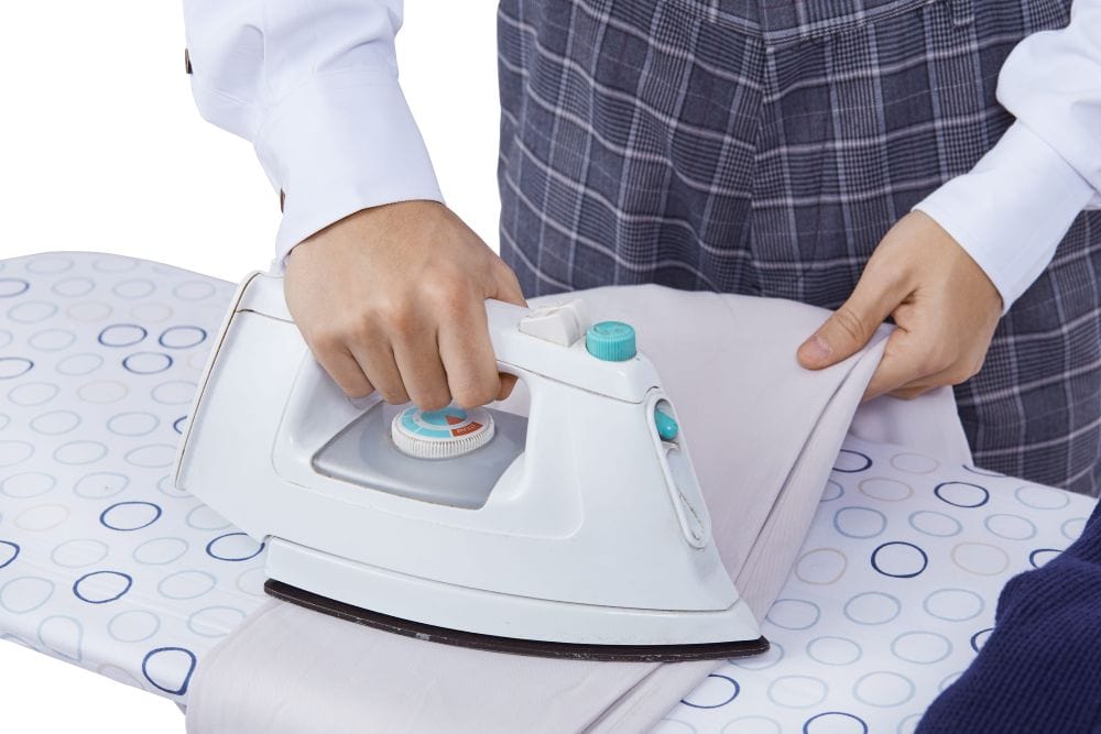 man uses an iron to get the wrinkles out of his linen suit pants