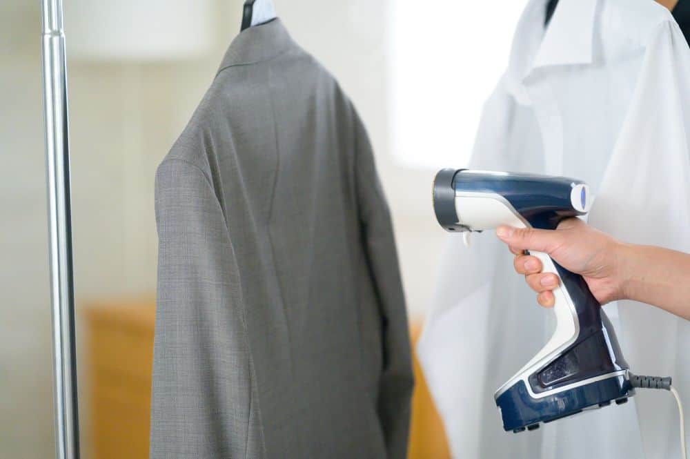 a man uses a garment steamer to rid his sportcoat of wrinkles