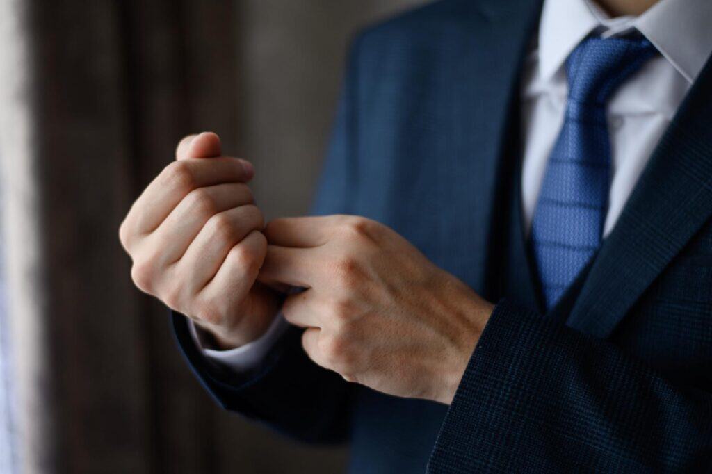A man in a navy suit and tie adjusting his cufflinks, following the cocktail dress code.