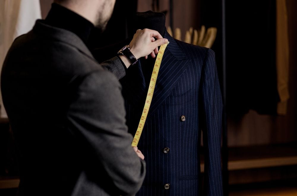 A tailor taking chest measurements for a suit fitting. Accurate measurements ensure the suit fits.
