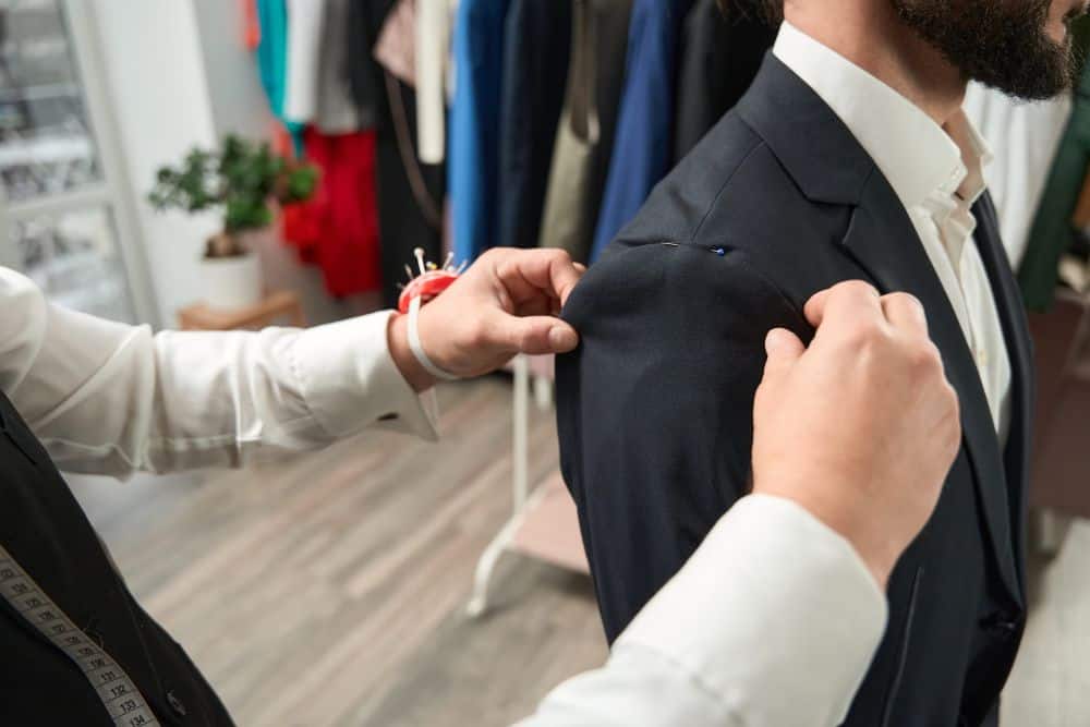 A tailor fitting a suit on a man preparing his wedding guest attiref