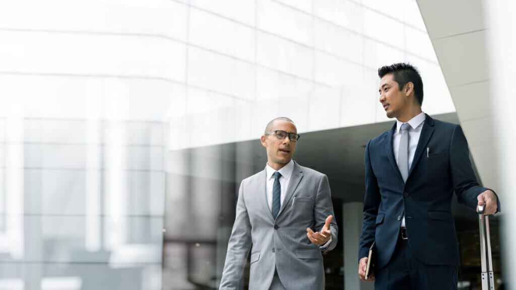 Two businessmen in notch lapel suits walking through an office building
