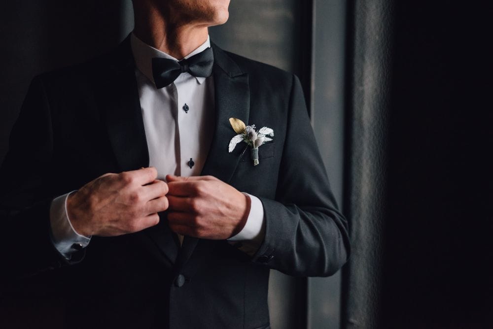 A man in a bespoke black tuxedo admires the master tailoring